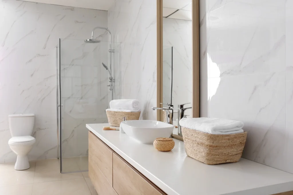 Modern bathroom featuring white quartz vanity countertops, vessel sink, light wood floating vanity, frameless glass shower, and marble-look wall panels in Knoxville, Tennessee.