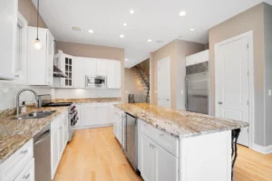 Bright kitchen with white cabinetry, a large granite island, and custom granite countertops installed in East Tennessee.
