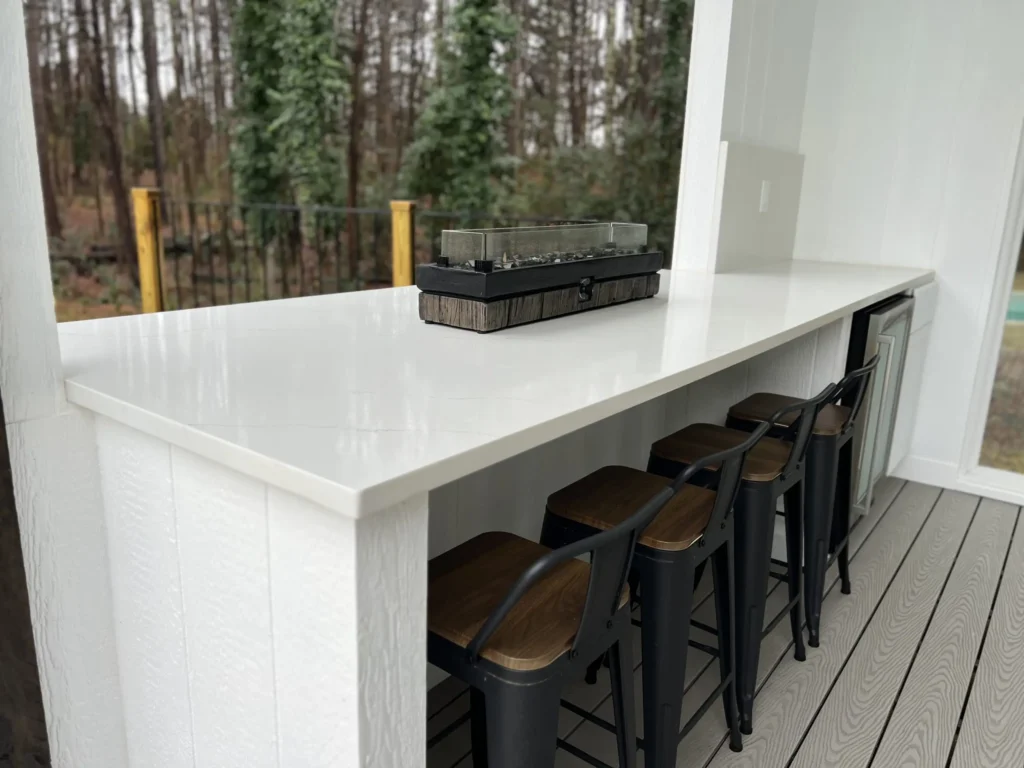 Covered outdoor kitchen with white quartz countertops in East Tennessee featuring bar seating and built-in appliances.