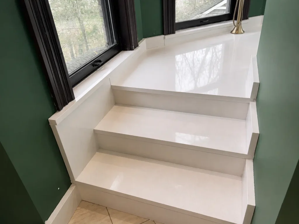 Modern white quartz staircase with polished stair treads and landing beside large windows, professionally fabricated and installed in Knoxville, Tennessee.
