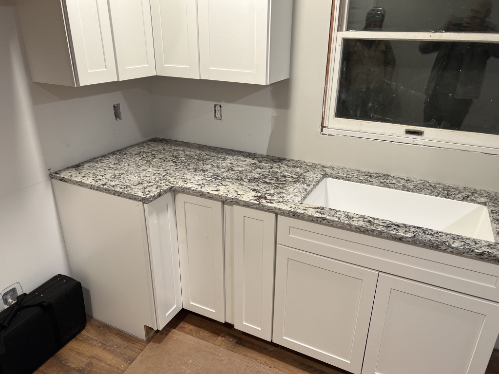 Dallas White granite countertop installed with white cabinets and farmhouse sink in a kitchen.