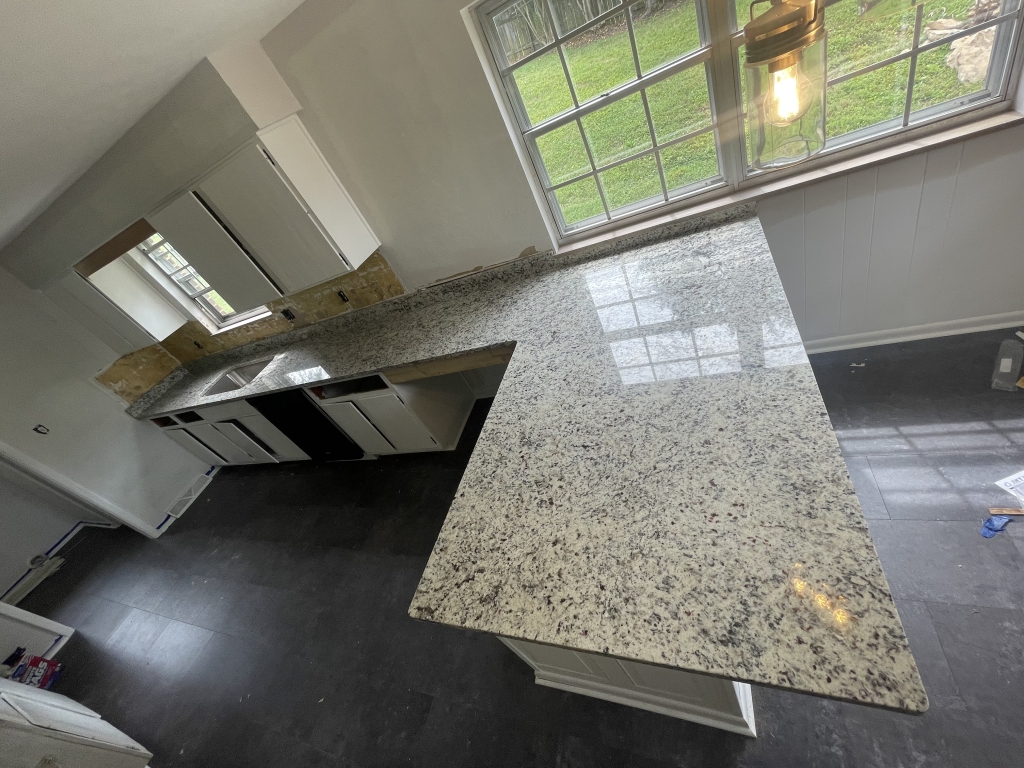 Moonlight granite countertops installed in a kitchen with a large peninsula and white cabinets.